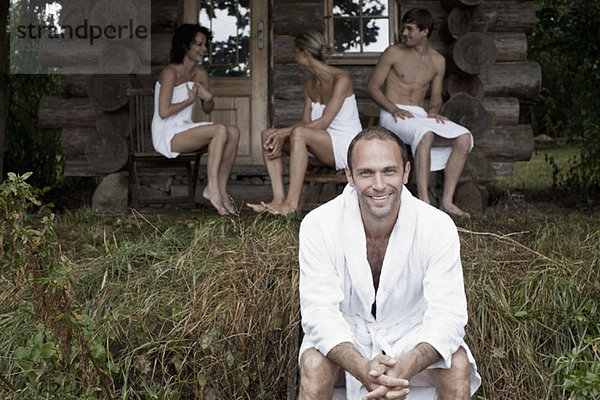 Ein Mann im Gras und drei Personen in Handtüchern im Hintergrund (Fokus auf Vordergrund)