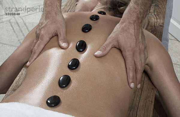 Ein Massagetherapeut  der die LaStone-Therapie an einer Frau durchführt.