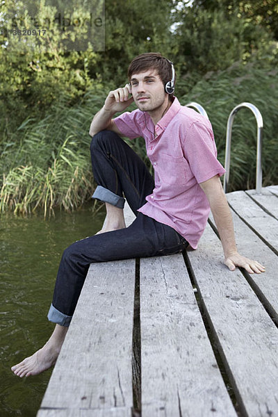 Ein Mann  der Kopfhörer trägt und sich an einem Steg entspannt.