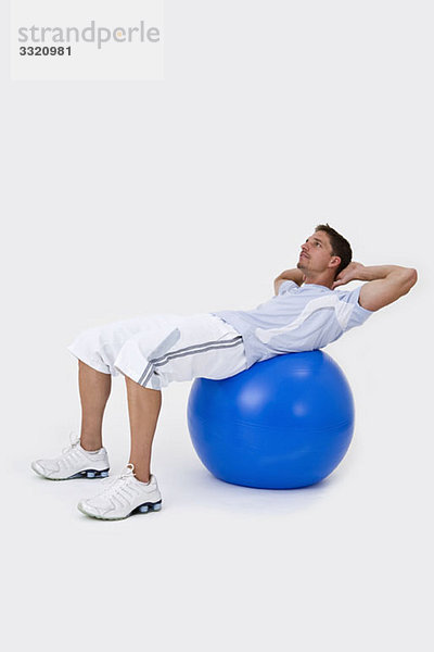 Ein Mann  der einen Übungsball benutzt  um Sit-ups zu machen.