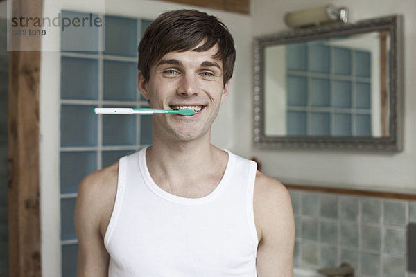 Ein Mann beißt auf eine Zahnbürste und lächelt.