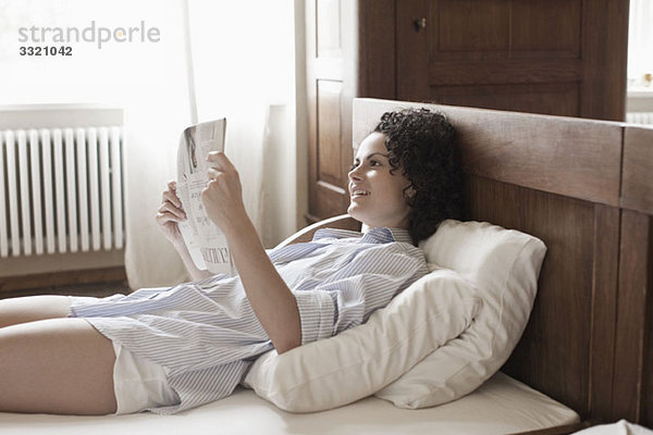 Eine Frau  die auf ihrem Bett liegt und die Zeitung liest.