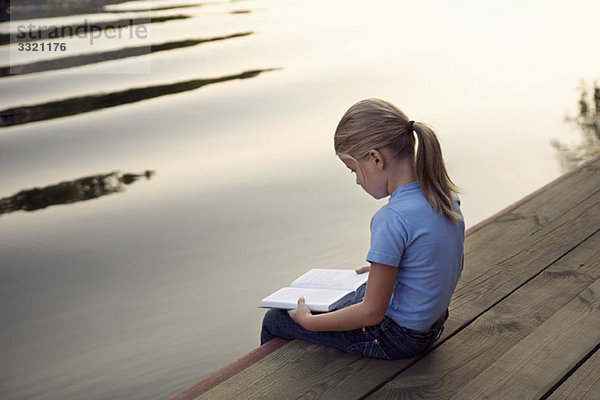 Ein junges Mädchen sitzt am Steg und liest ein Buch.