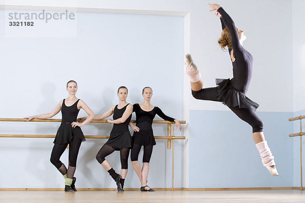 Eine Ballerina  die durch die Luft springt  während drei andere Frauen zusehen.