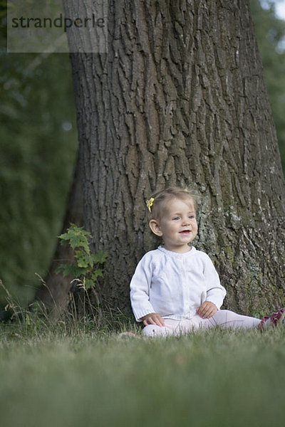 Ein kleines Mädchen sitzt unter einem Baum und schaut weg.