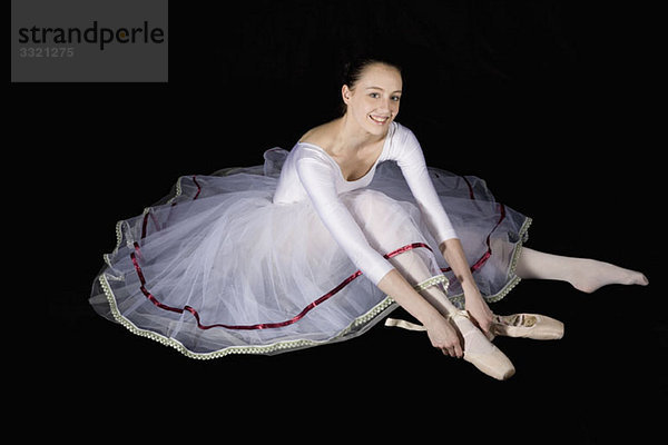 Eine lächelnde Balletttänzerin  die ihren Spitzenschuh anzieht.