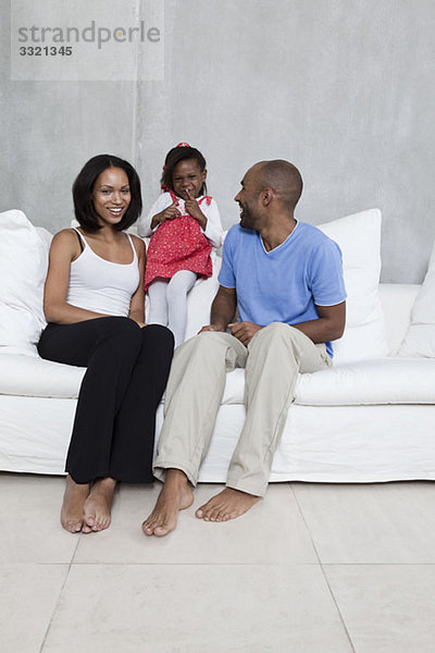 Eine junge Familie  die gemeinsam auf dem Sofa lacht.