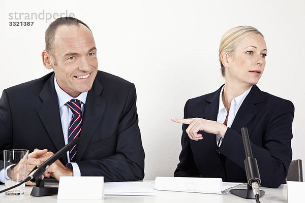 Ein Mann und eine Frau sitzen an einem Schreibtisch mit Mikrofonen.