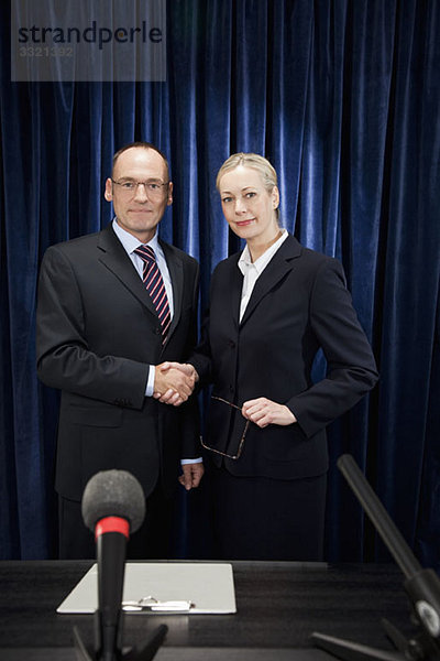 Ein Mann und eine Frau geben sich bei einer Pressekonferenz die Hand.