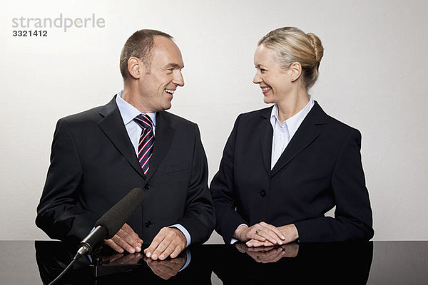 Ein Mann und eine Frau sitzen am Schreibtisch mit einem Mikrofon.