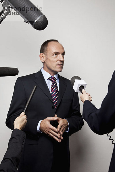 Ein Mann in einem Anzug  der von den Medien interviewt wird.