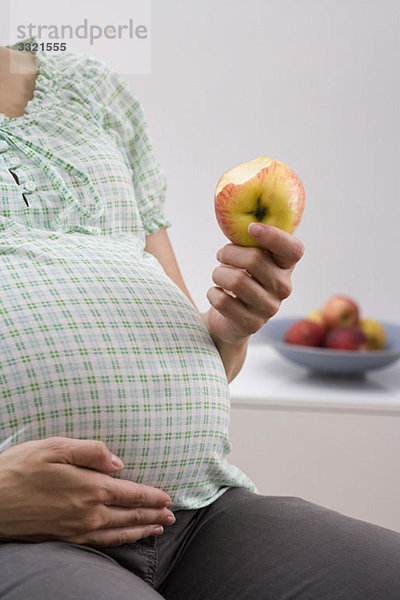 Eine schwangere Frau beim Essen eines Apfels  Mittelteil