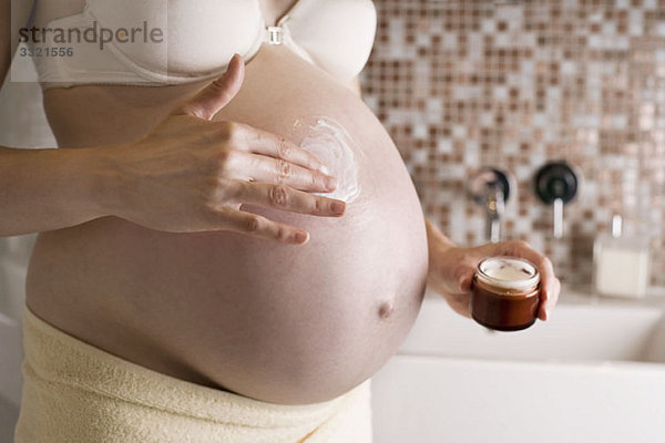 Eine schwangere Frau  die Feuchtigkeitscreme an ihrem Bauch reibt  Mittelteil