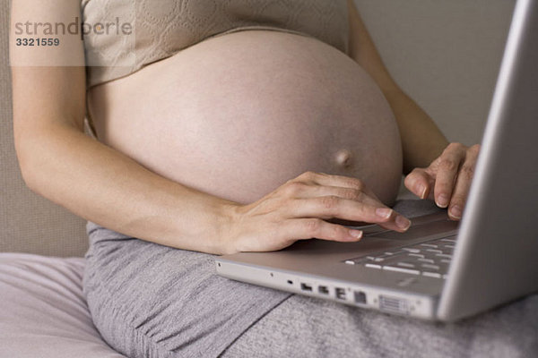 Eine schwangere Frau mit einem Laptop  Mittelteil  Konzentration auf die Hände