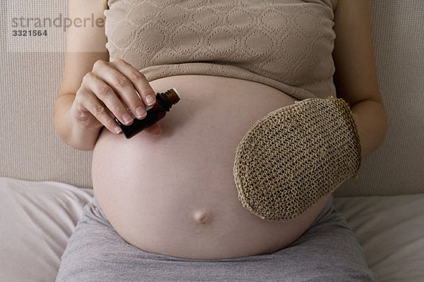 Eine schwangere Frau  die Körperöl auf ihren Magen aufträgt  Mittelteil