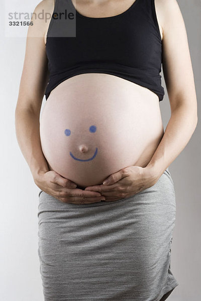 Ein Smiley auf einen schwangeren Bauch gezeichnet  Mittelteil  Fokus auf den Bauch