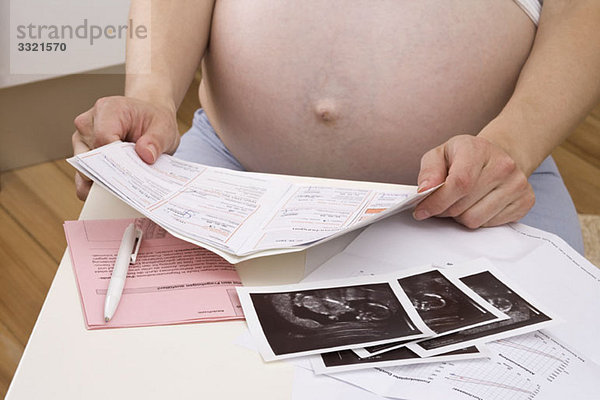 Eine schwangere Frau  die sich den medizinischen Papierkram und die Ultraschalluntersuchung ansieht.
