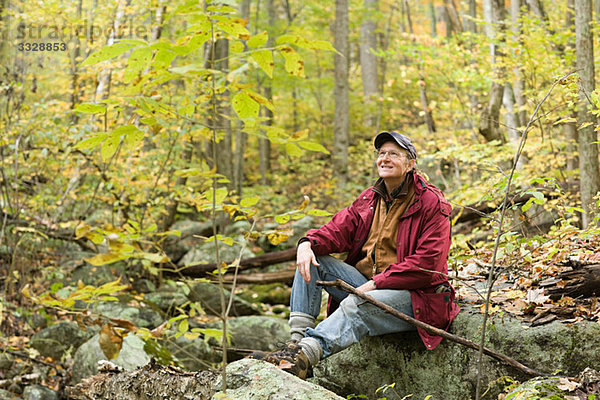 Ein Mann sitzt auf einem Felsen im Wald.