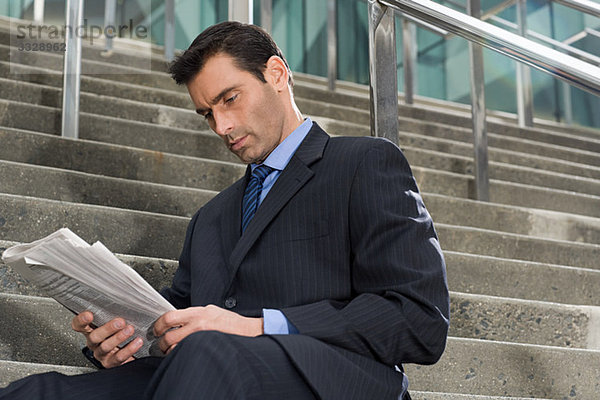 Ein Geschäftsmann  der mit einer Zeitung auf einer Treppe sitzt.