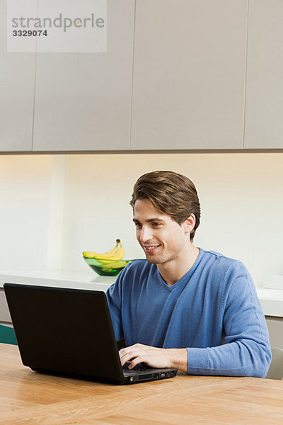 Junger Mann am Tisch sitzend mit Laptop