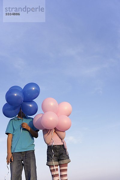 zwei Kinder versteckt hinter Luftballons