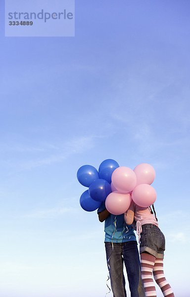 zwei Kinder versteckt hinter Luftballons