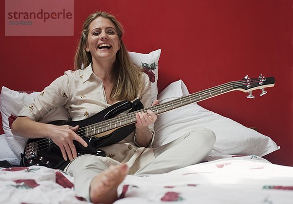 Frau spielt Gitarre auf dem Bett