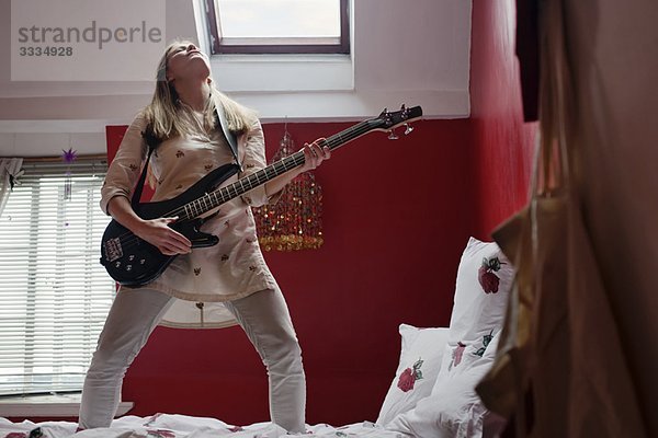 Frau spielt Gitarre auf dem Bett