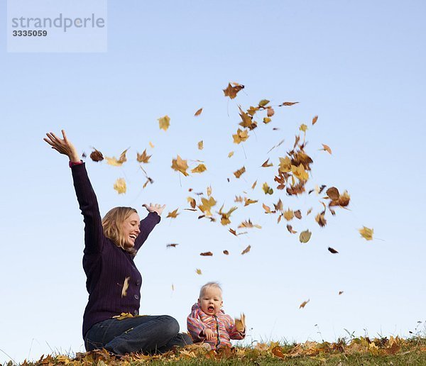 Mutter und Baby werfen Herbstlaub