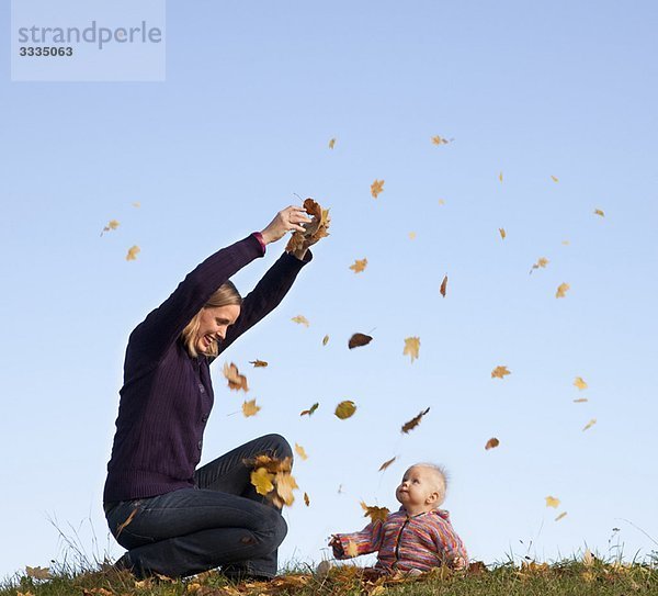 Mutter und Baby werfen Herbstlaub