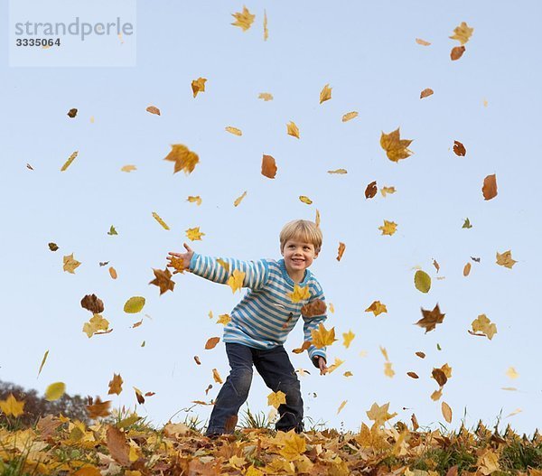 Junge wirft Herbstlaub in die Luft