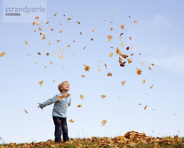 Junge wirft Herbstlaub in die Luft