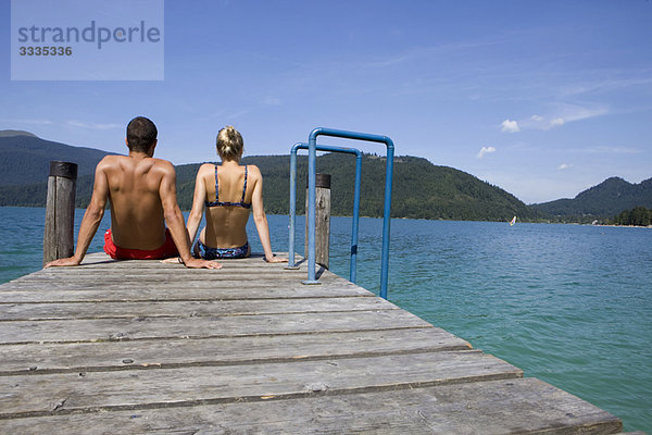 Ein Paar sitzt auf einem Pier am See.