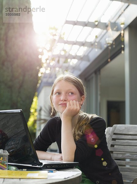 Junges Mädchen denkt am Laptop im Garten