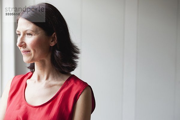 Frau in rotem Kleid am Fenster stehend