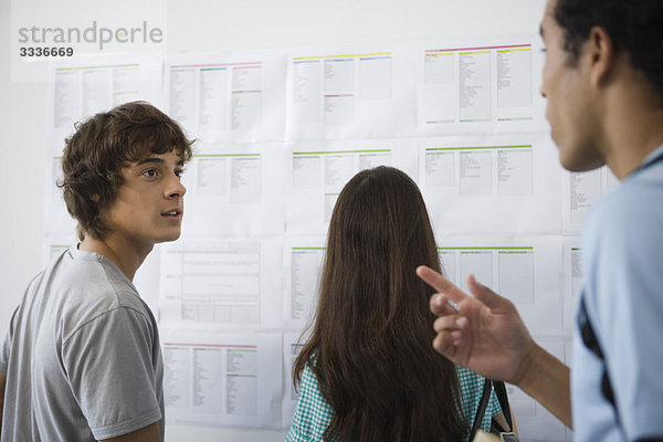 Studenten chatten  Studentinnen checken das Schwarze Brett im Hintergrund