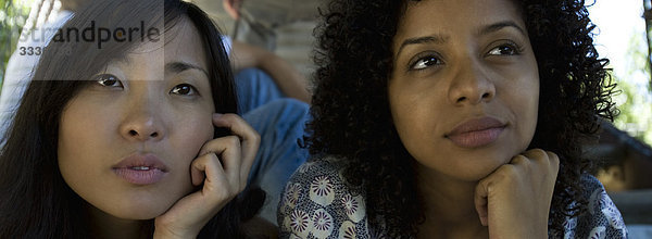 Zwei junge Frauen sitzen zusammen im Freien  beide schauen weg und träumen.