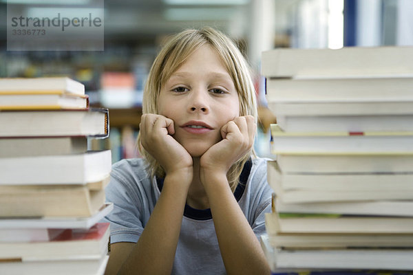 Junge  der sich auf den Ellenbogen lehnt  mit Blick auf Langeweile  Bücherstapel im Vordergrund