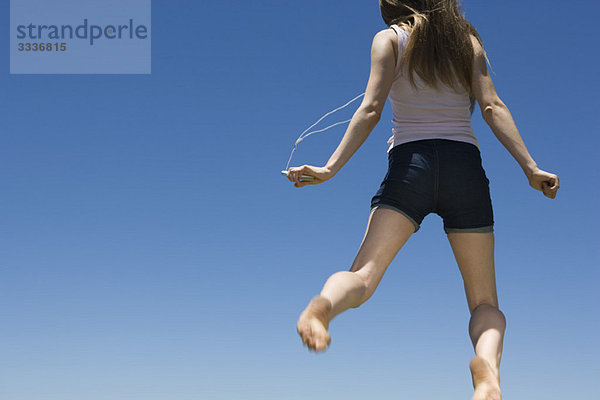 Junge Frau hörtMP3-Player  springt in der Luft