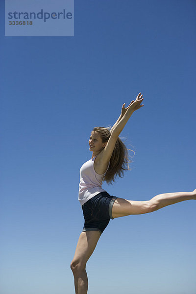 Junge Frau mit erhobenen Armen  auf einem Bein balancierend