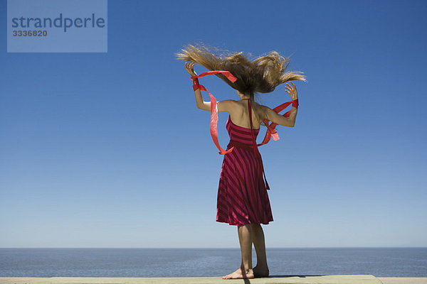 Junge Frau am Strand mit Blick auf die Aussicht  hält Luftschlangen im Wind