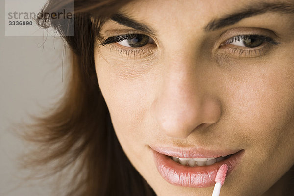 Junge Frau beim Auftragen von Lippenglanz mit Lippenpinsel und Mund