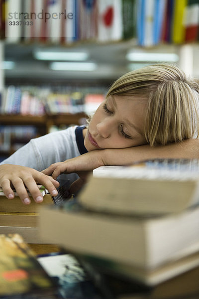 Junge ruht Kopf auf den Armen schlafend in der Bibliothek