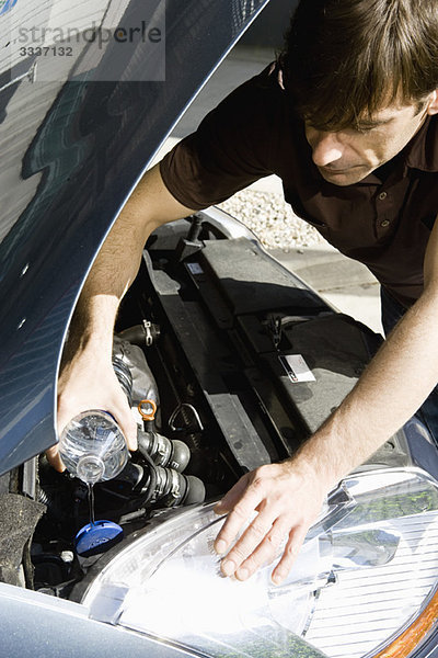 Mann gießt Wasser in den Kühler eines überhitzten Autos