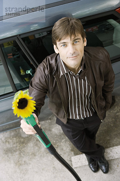 Mann an der Tankstelle hält Gasdüse mit austretender Sonnenblume