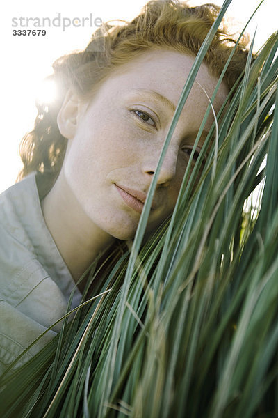Frau mit Gesicht gegen hohes Gras gepresst mit Blick auf die Kamera