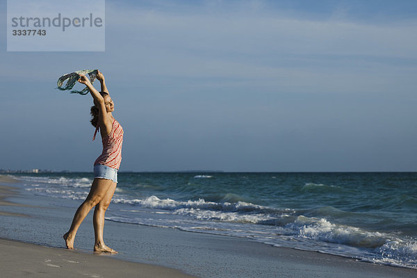 Frau hält Schal im Wind am Strand hoch  Augen geschlossen