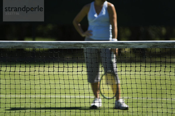 Tennisplatznetz  Tennisspieler mit Hand auf Hüfte im Hintergrund