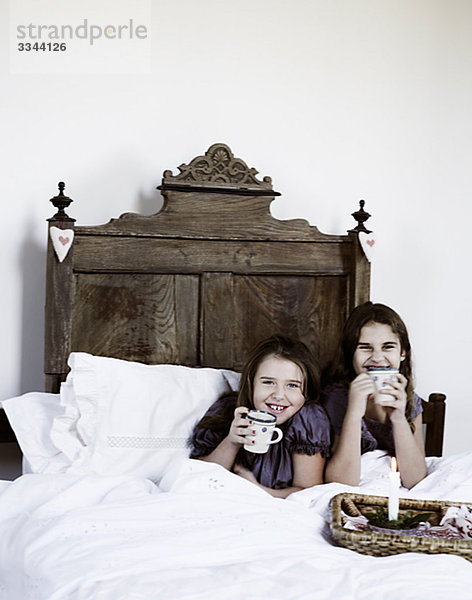 Zwei Mädchen mit eine Tasse heißer Schokolade in einem rustikalen Bett  Italien.