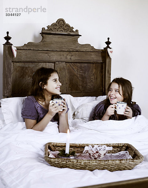 Zwei Mädchen mit eine Tasse heißer Schokolade in einem rustikalen Bett  Italien.